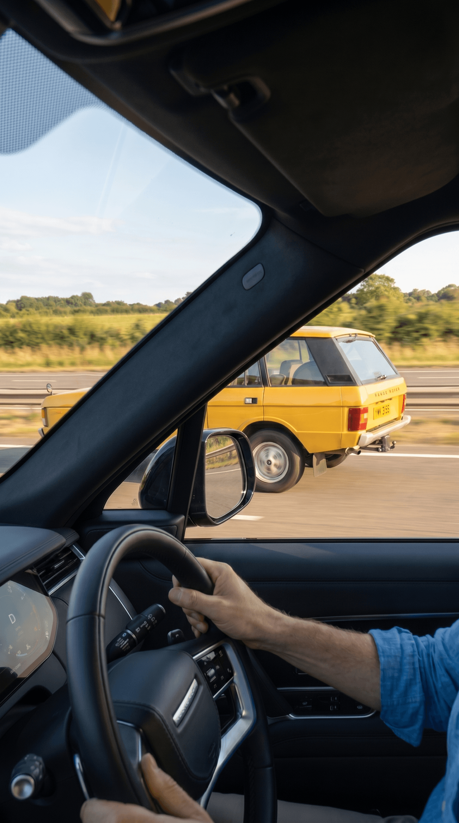 View through a UK car windscreen of a Monte Carlo Yellow classic Range Rover passing on the motorway, the driver looking across as a car they used to own goes by